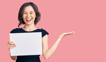 Fototapeta premium Young beautiful girl holding blank empty banner celebrating victory with happy smile and winner expression with raised hands