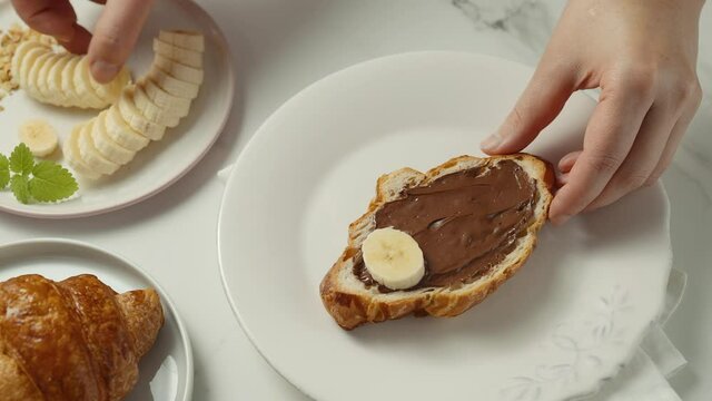 A young girl decorates a banana croissant with chocolate paste