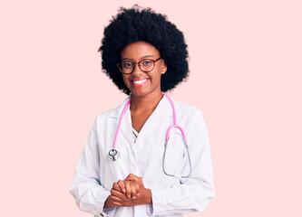 Young african american woman wearing doctor coat and stethoscope with hands together and crossed fingers smiling relaxed and cheerful. success and optimistic