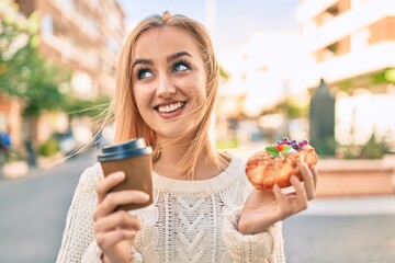 Young blonde girl smiling happy having breakfast standing at the city.