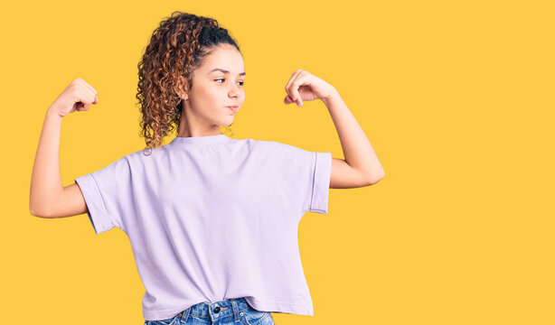 Beautiful kid girl with curly hair wearing casual clothes showing arms muscles smiling proud. fitness concept.