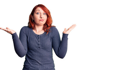 Young beautiful redhead woman wearing casual t-shirt clueless and confused expression with arms and...