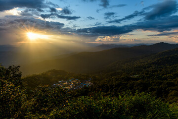 The bright rays of the sun are shining from saturated clouds to mountain range before sunset.