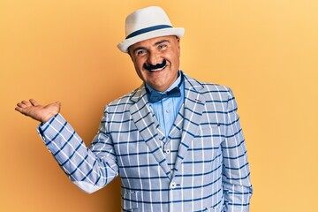 Mature middle east man with mustache wearing vintage and elegant fashion style smiling cheerful presenting and pointing with palm of hand looking at the camera.