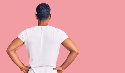Young latin man wearing casual clothes standing backwards looking away with arms on body