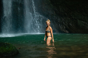 Young Caucasian woman with blond hair standing near the waterfall. Travel lifestyle. Leke Leke waterfall, Bali.