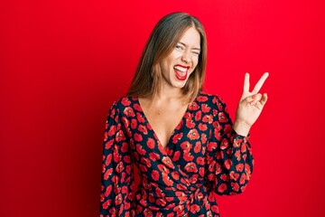 Beautiful young blonde woman wearing elegant dress smiling with happy face winking at the camera doing victory sign. number two.