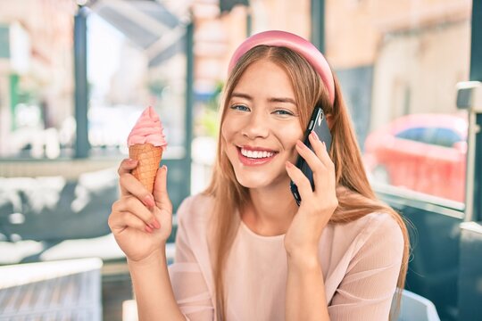 Young caucasian girl talking on the smartphone and eating ice cream sitting at terrace.