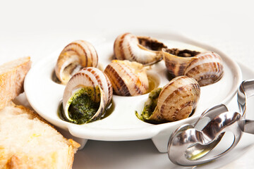 snail dish, served on a white classic plate, with various sauces (pesto, truffle, cheese), pieces of French baguette, fork for a shell, wooden table, from close range, space, horizontal, no one
