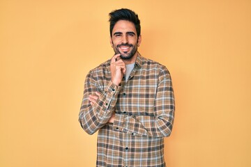 Fototapeta premium Handsome hispanic man with beard wearing casual clothes looking confident at the camera with smile with crossed arms and hand raised on chin. thinking positive.