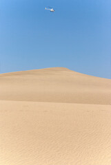 Helicopter flies over the desert landscape in the dunes of Maspalomas, Gran Canaria, Canary Islands, Spain