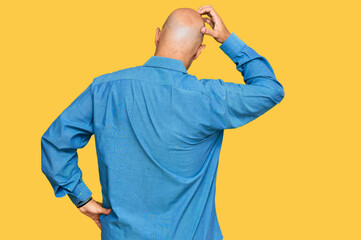 Middle age bald man wearing casual clothes backwards thinking about doubt with hand on head