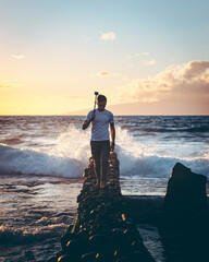 A person walking on a wall as the waves crash behind him