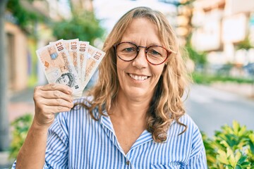 Middle age caucasian woman smiling happy holding uk pounds banknotes standing at the city.