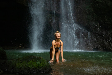 Fototapeta premium Young Caucasian woman with blond hair standing near the waterfall. Travel lifestyle. Leke Leke waterfall, Bali.