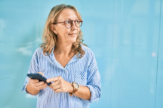 Middle age caucasian woman smiling happy using smartphone at the city.