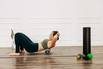 Adult sporty woman doing fascia exercise on the floor. Caucasian female using foam massage roller - tool for back tension and muscle pain release. training stretch concept