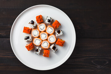 Top view - set of various sushi on white plate on wooden table background. Rolls of philadelphia and other. Copy space.