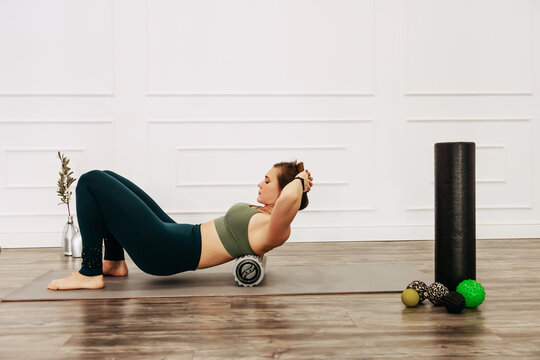 Adult sporty woman doing fascia exercise on the floor. Caucasian female using foam massage roller - tool for back tension and muscle pain release. training stretch concept