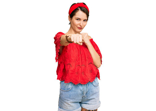 Young brunette woman with short hair wearing casual summer clothes and diadem punching fist to fight, aggressive and angry attack, threat and violence