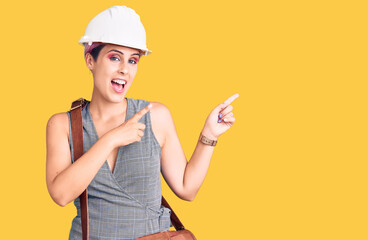 Young beautiful woman wearing architect hardhat and leather bag smiling and looking at the camera pointing with two hands and fingers to the side.