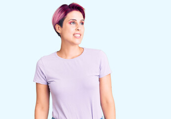 Young beautiful woman with pink hair wearing casual clothes looking away to side with smile on face, natural expression. laughing confident.