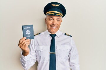 Handsome middle age mature pilot man holding usa passport looking positive and happy standing and...