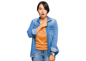 Fototapeta premium Young beautiful hispanic woman with short hair wearing casual denim jacket surprised pointing with finger to the side, open mouth amazed expression.