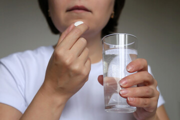 Woman in white top taking pill holding a water glass. Concept of medication or vitamins