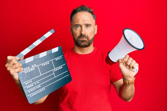 Handsome middle age man holding video film clapboard and megaphone depressed and worry for distress, crying angry and afraid. sad expression.