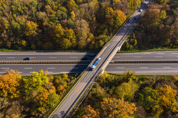 Luftaufnahme einer Brücke über eine Autobahn mit viel Verkehr die sich durch einen herbstlichen...