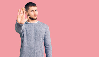 Young handsome man wearing casual sweater doing stop sing with palm of the hand. warning expression...