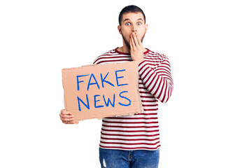 Young handsome man holding fake news message banner covering mouth with hand, shocked and afraid...