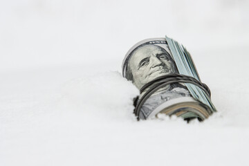 A dollar in winter, a roll of twisted dollar bills lying on the snow, close-up.