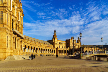 Fototapeta premium Plaza de España en Sevilla al atardecer en un día soleado con nubes y gente paseando y disfrutando del buen tiempo.
