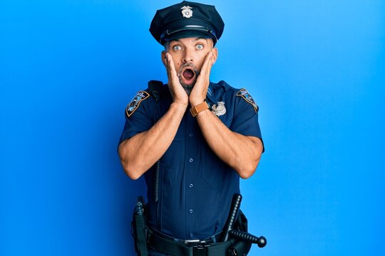 Middle age handsome man wearing police uniform afraid and shocked, surprise and amazed expression with hands on face