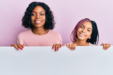 Beautiful african american mother and daughter holding blank empty banner looking positive and...