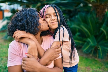 Beautiful african american mother and daughter kissing and hugging. Standing with smile on face standing at the park.