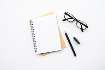 Blank notebook is on top of white office desk table with pen and eye glasses. Top view, flat lay.