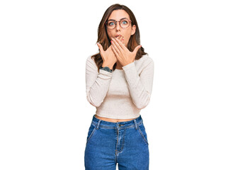 Young brunette woman wearing casual clothes and glasses shocked covering mouth with hands for mistake. secret concept.