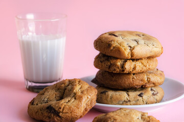Stack of chocolate chip cookies beside a glass of milk in front of a pink background