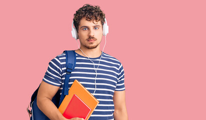 Young handsome man with curly hair holding student backpack and books thinking attitude and sober expression looking self confident