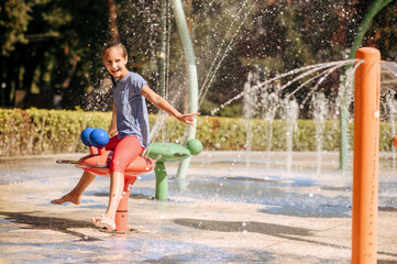 Happy little girl in splashes on water playground