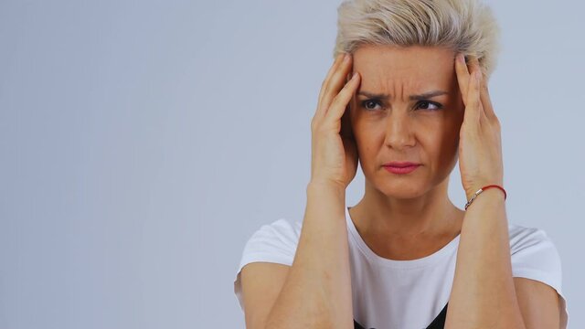 Blond adult woman close-up on white background rubs whiskey. She's got headache. Model smurs her forehead and lowers her eyes. Place under copy space. High quality 4k footage