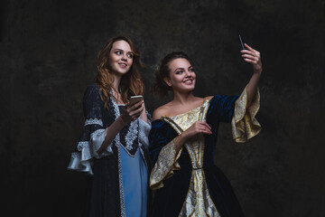 Two happy women in renaissance dress taking selfie on smartphone, old and new concept