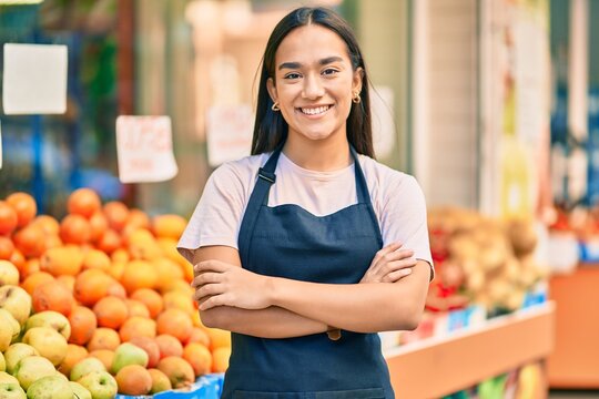 Young latin shopkeeper girl with arms crossed smiling happy at the fruit store.