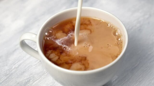Adding milk to a cup of black tea. White and brown swirling. Closeup. Slow motion. Rotation. Abstract chaotic movement