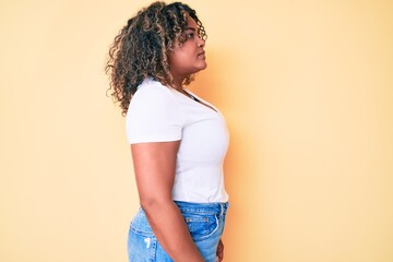 Young african american plus size woman wearing casual white tshirt looking to side, relax profile pose with natural face with confident smile.