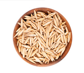 Unpeeled oat grains in wooden bowl, isolated on white background. Organic dry oat seeds. Top view.