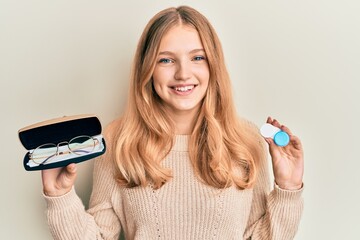 Beautiful young caucasian girl holding glasses and contact lenses smiling with a happy and cool...